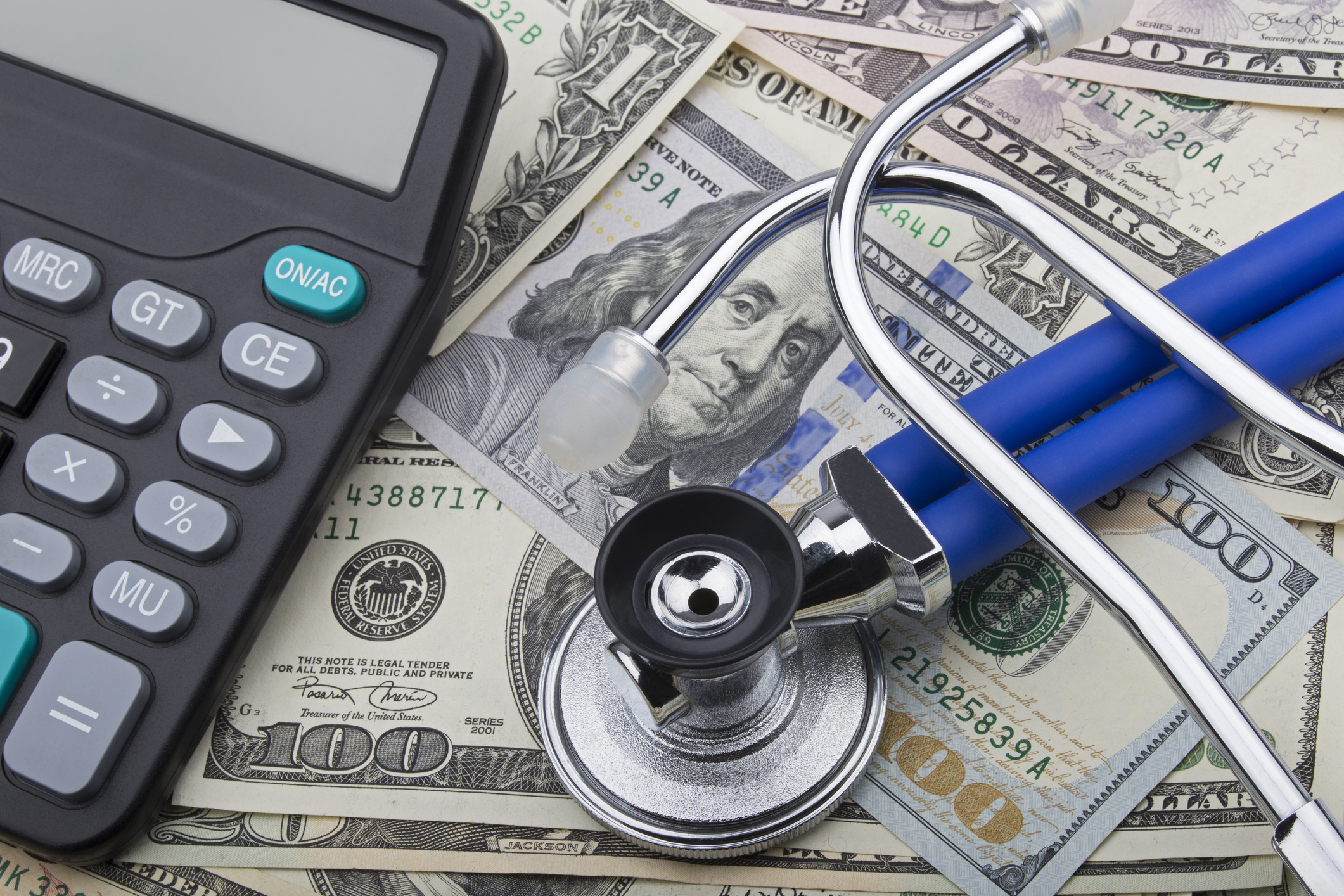 A calculator and a stethoscope on a pile of cash.