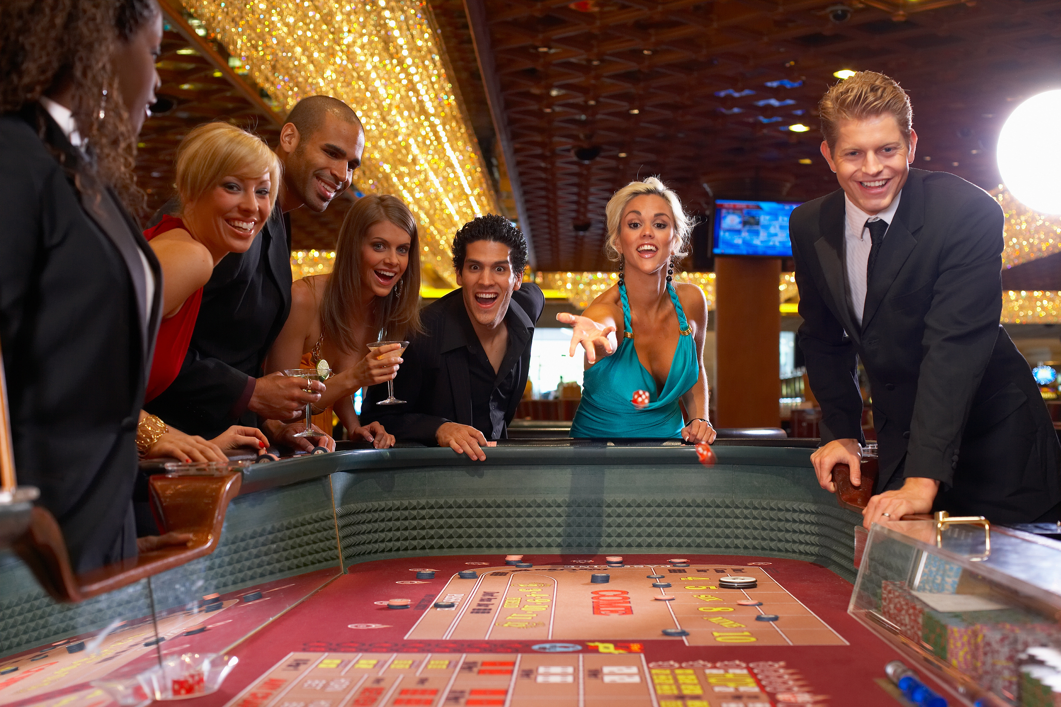 Well-dressed people smiling at a craps table with a woman throwing dice.