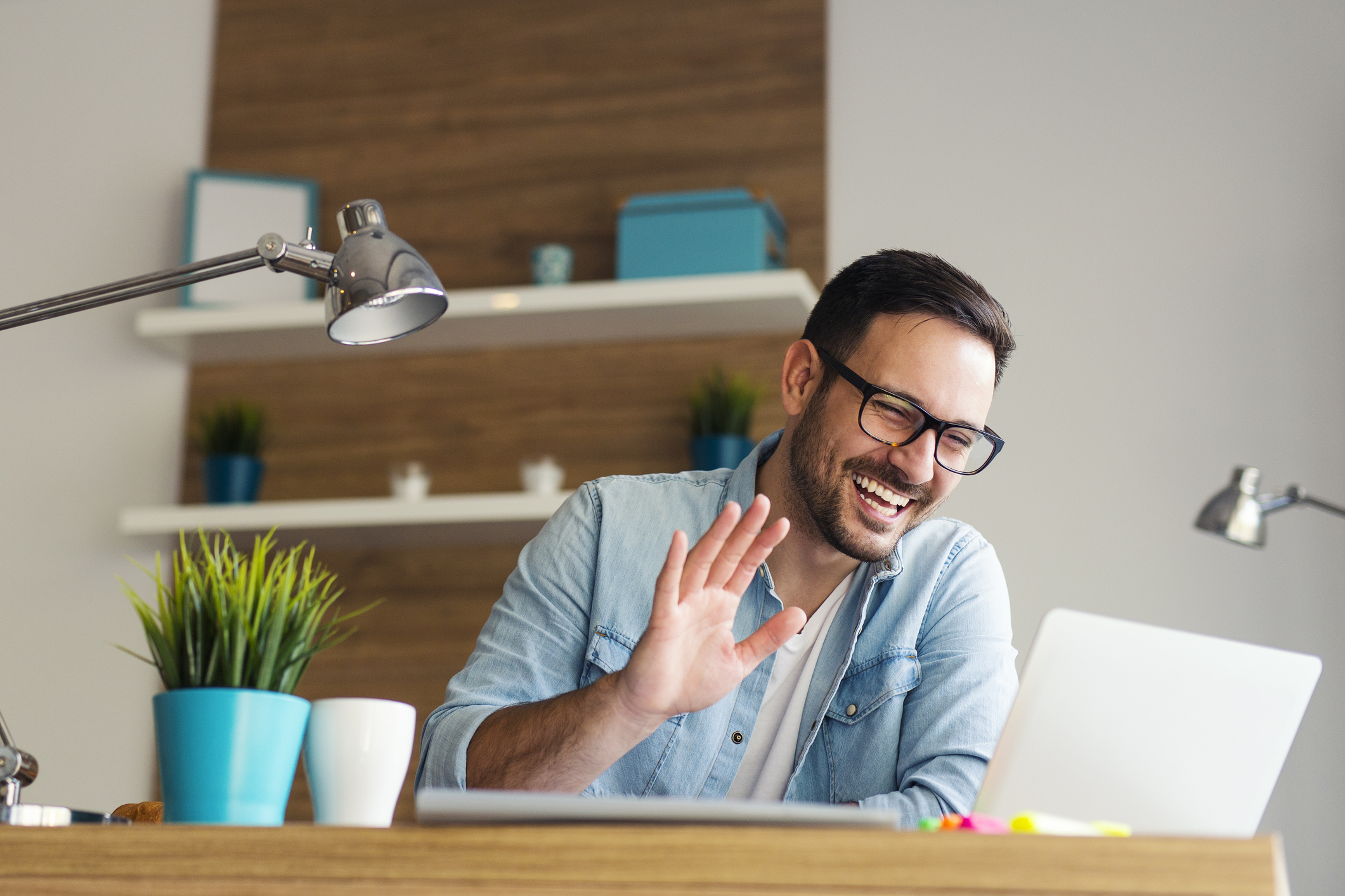 A smiling young man waving at the screen of a laptop computer