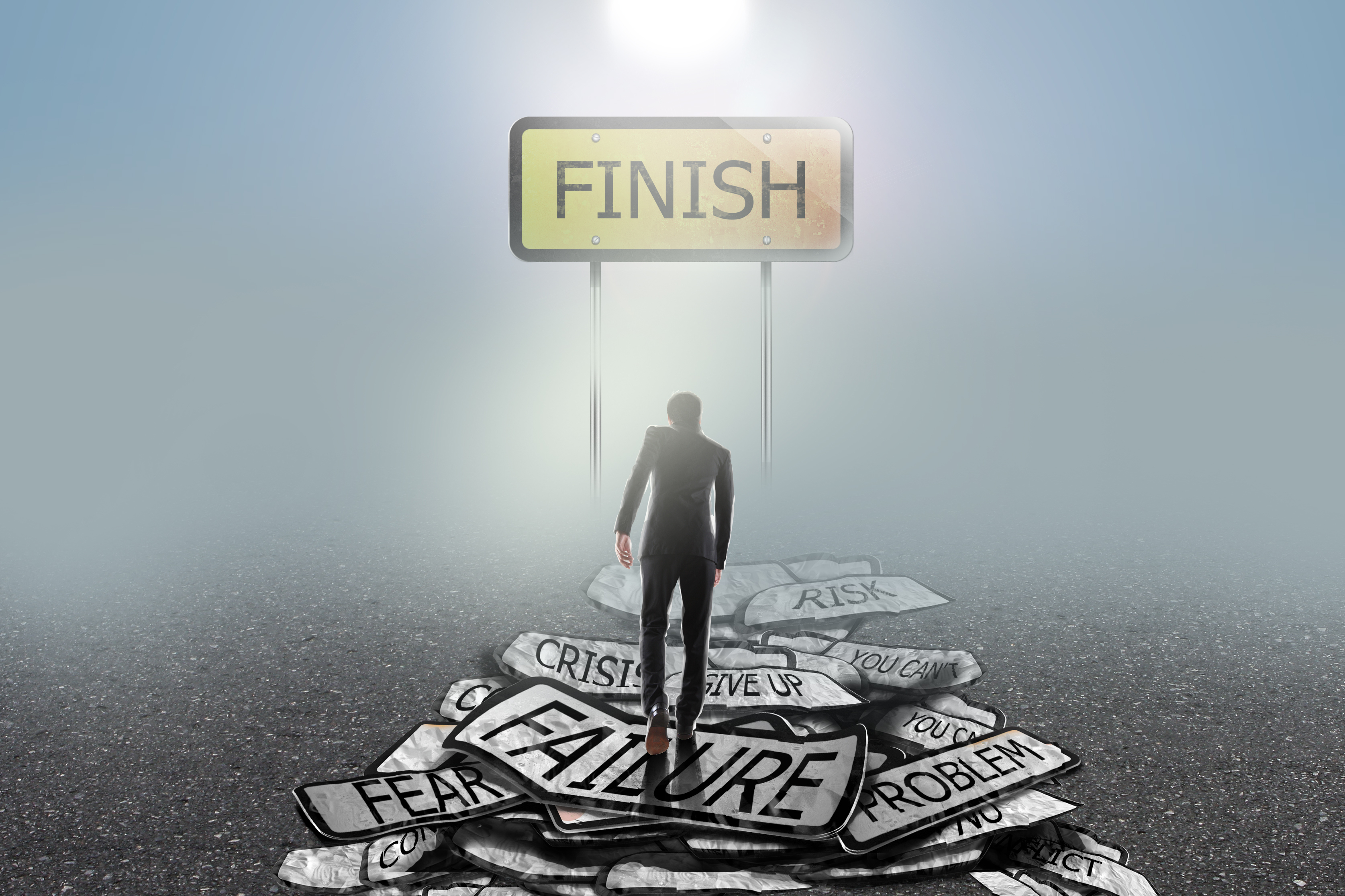 A man in a suit climbing a mountain of failure signs toward a finish line.