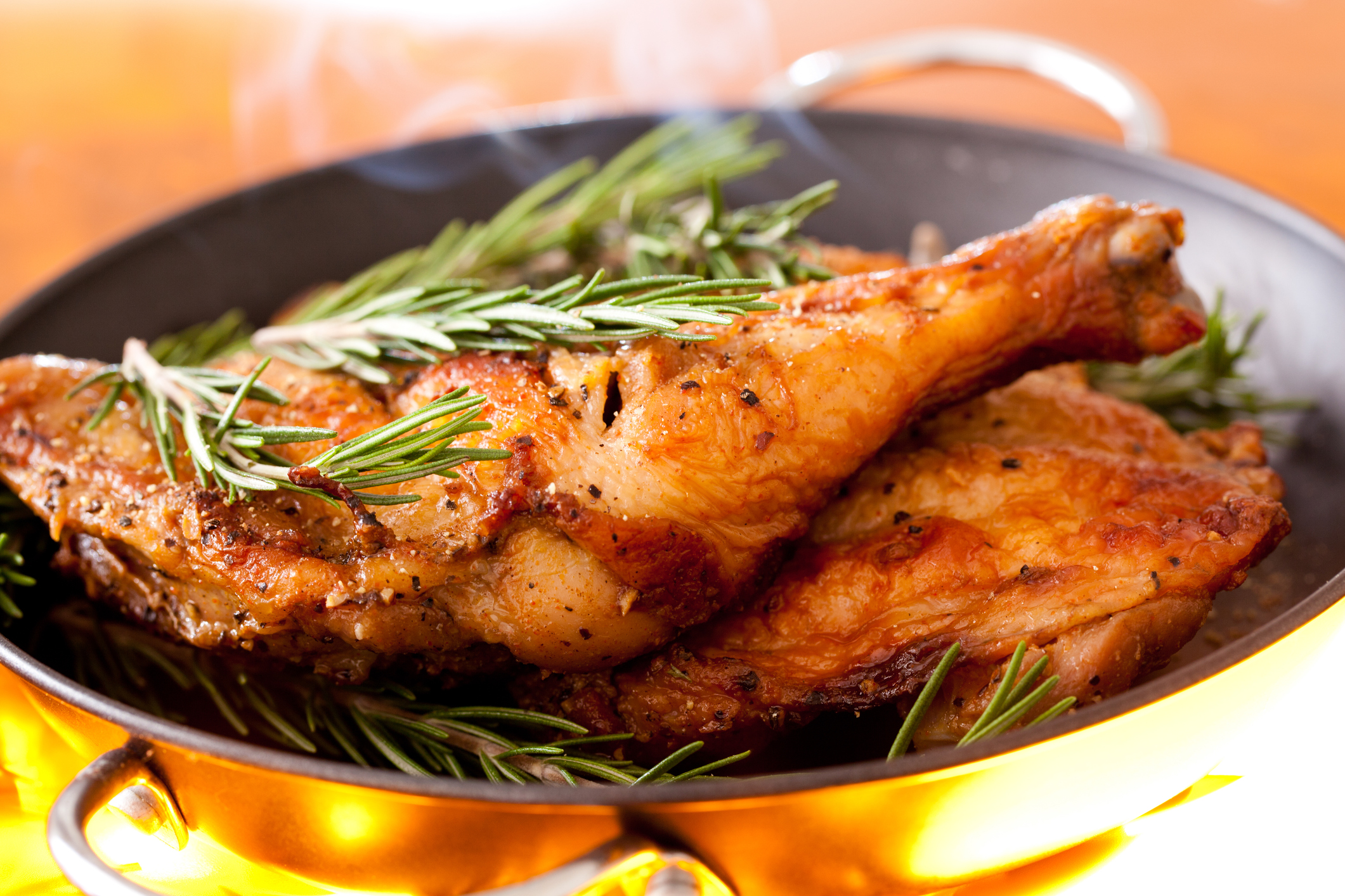Roasted chicken in a pan, topped with rosemary.