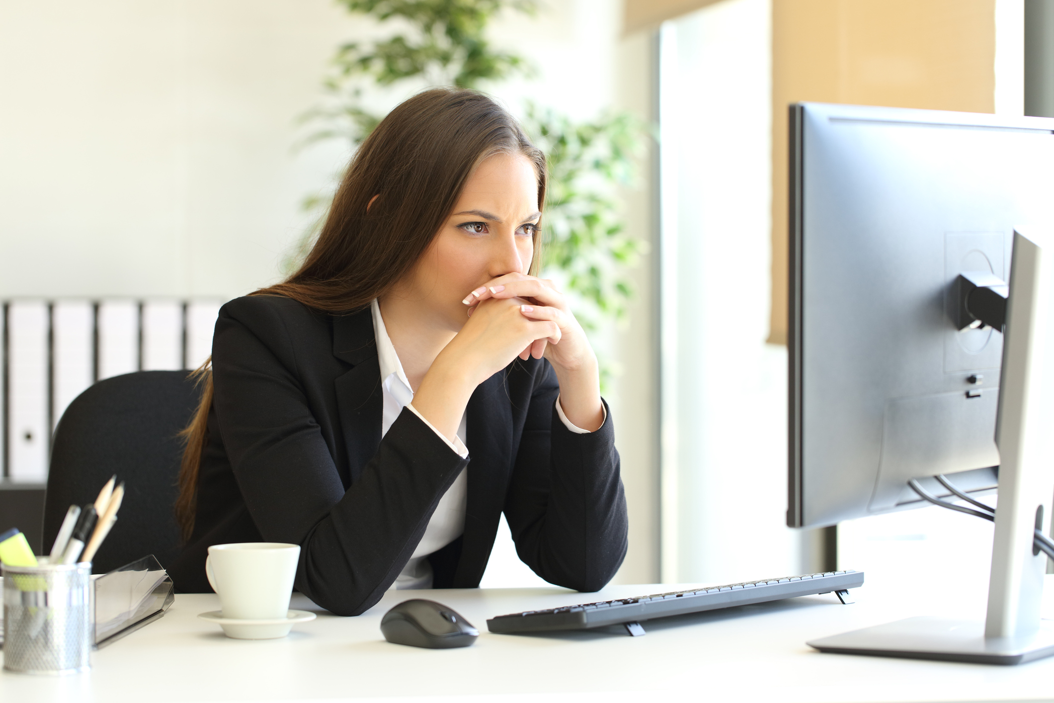Worried-looking woman in a suit looking at a computer screen.