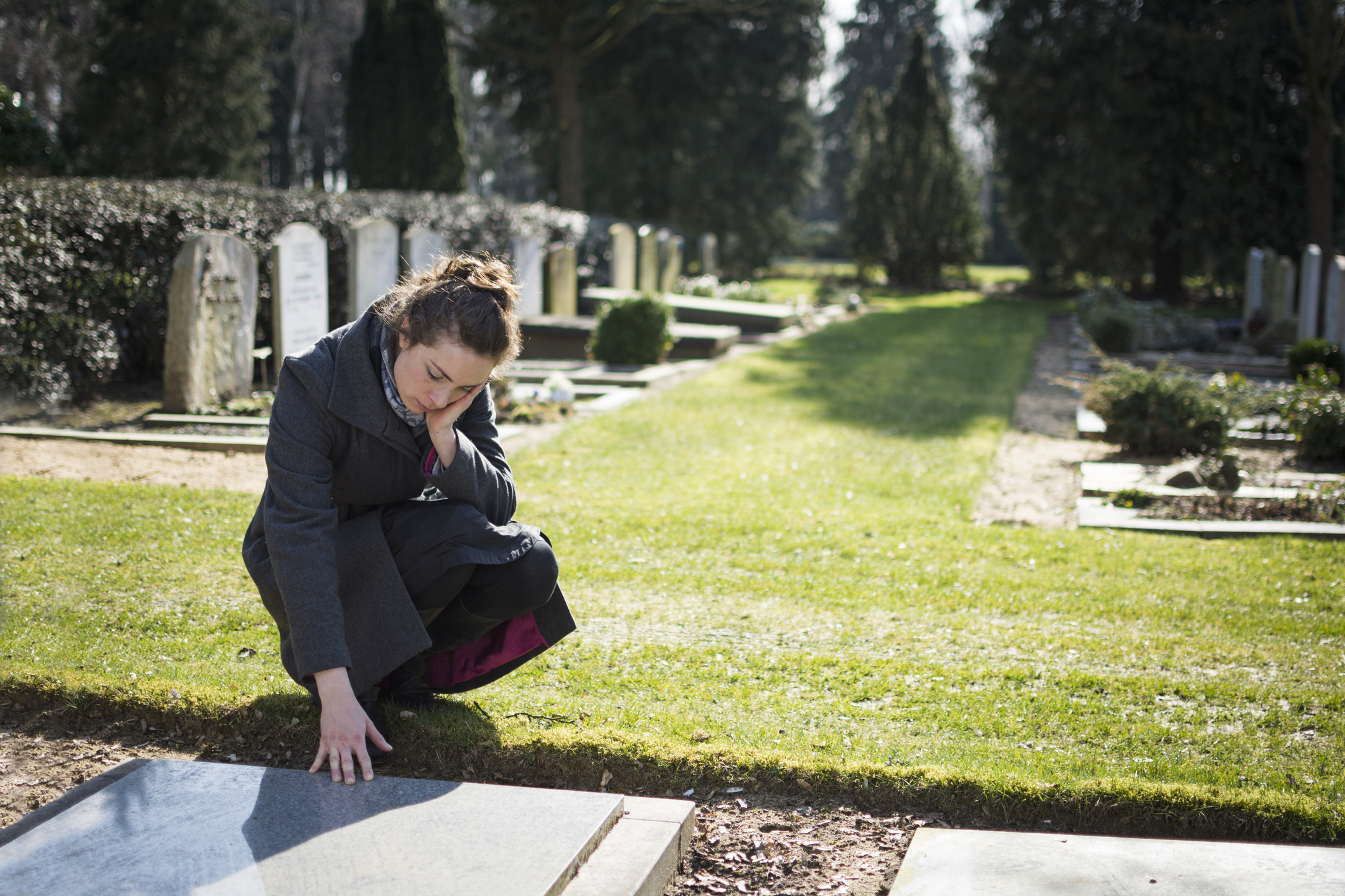 Woman kneeling down and putting her hand on a grave
