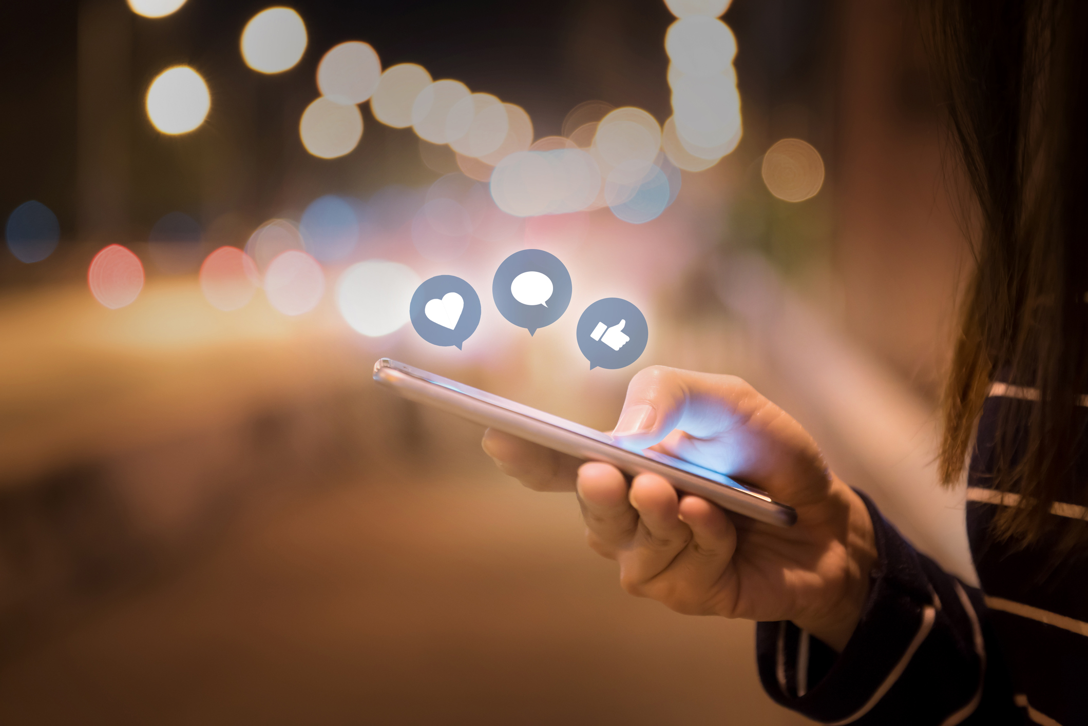 Woman hands using mobile smartphone on the street with social media icons hovering above it.
