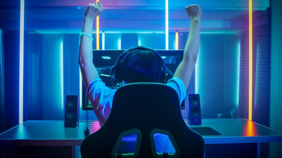 A person in a chair looking at a monitor and raising their arms in the air.