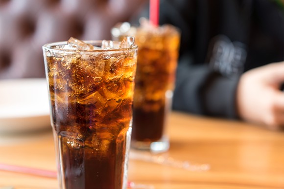 Two glasses of soda on a table, with a person sitting in the background.