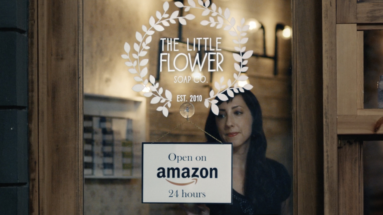 A woman stands in front of a sign touting that her store is open 24 hours on Amazon.