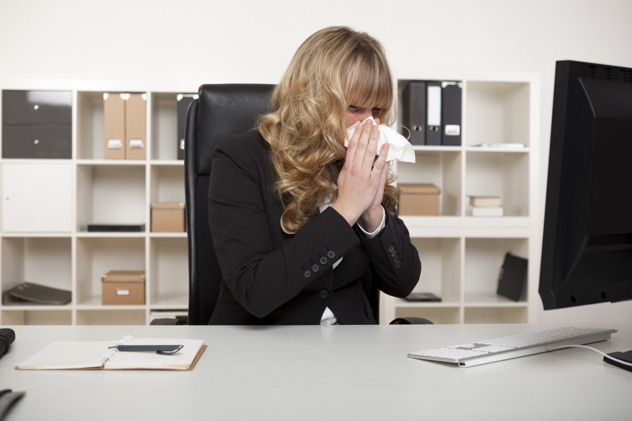 Woman blowing nose at her desk