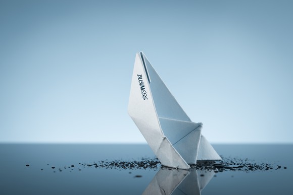 Paper boat sinking into a black liquid.