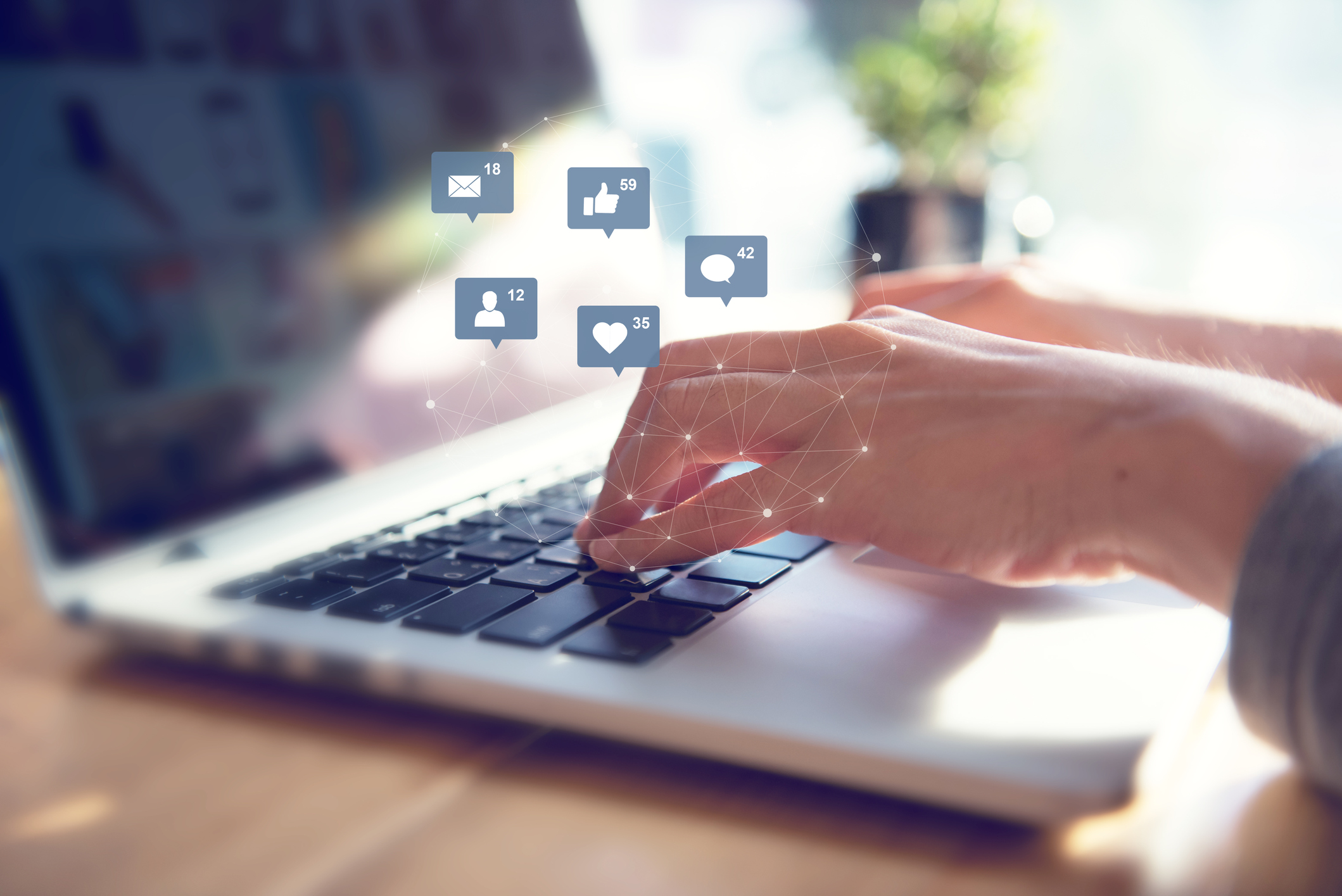 Hands typing on a laptop with social media icons floating above it.
