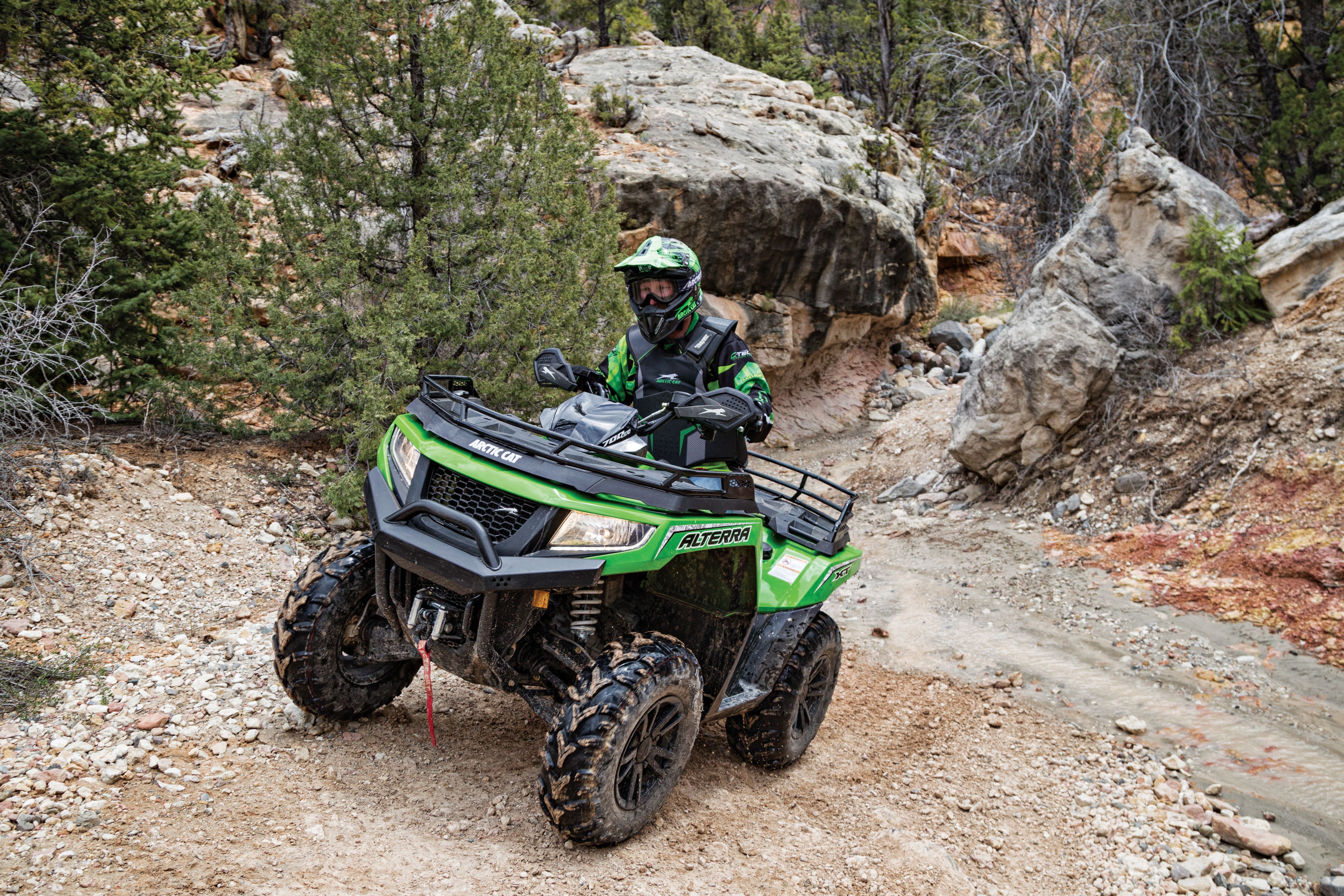 Man in full gear riding an ATV up a dirt incline