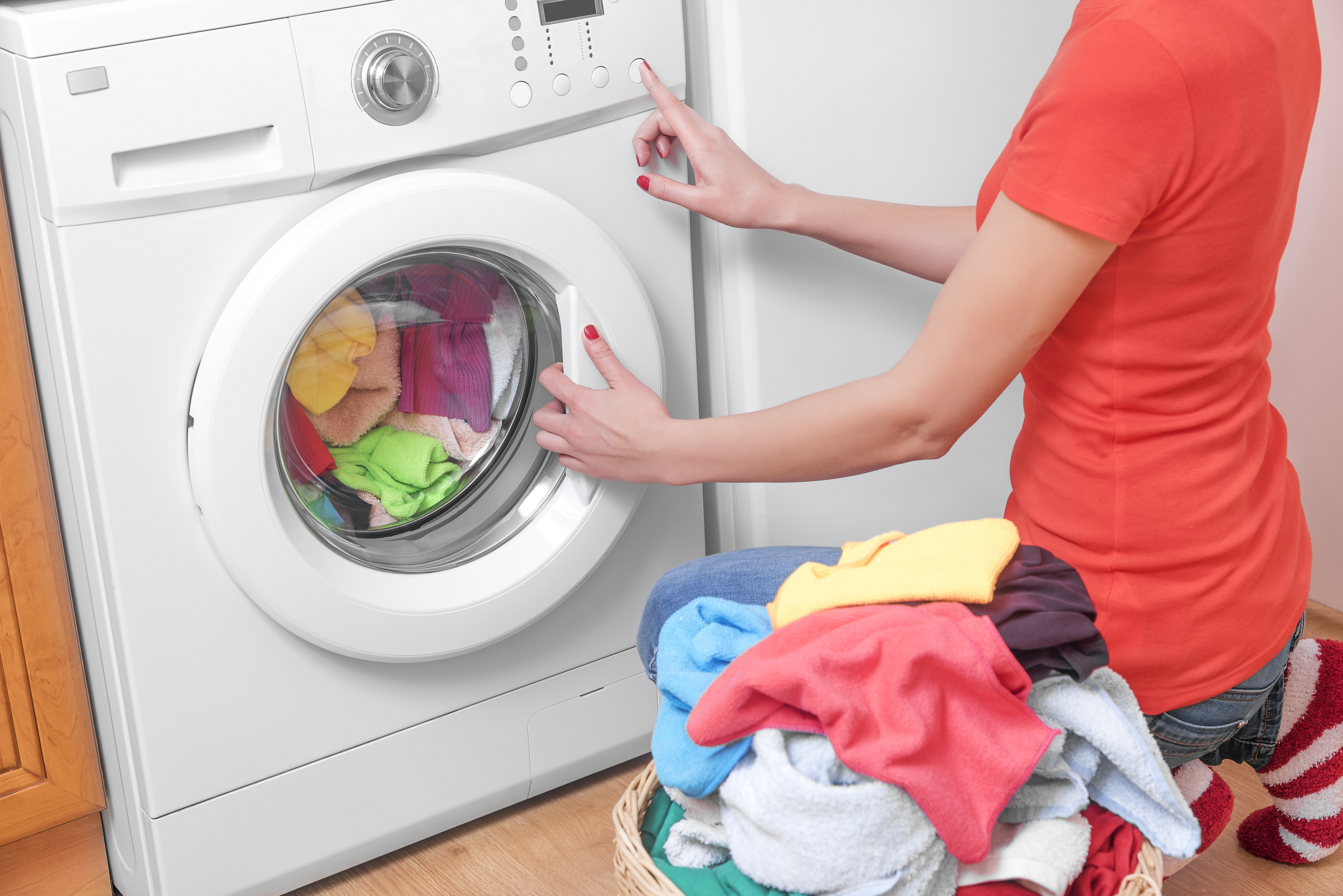 A woman putting wet clothes into a dryer, with a basket of clean clothes to her left. 