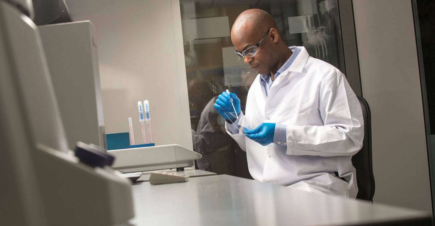 Scientist in white lab coat with blue gloves working on Corning glass products.