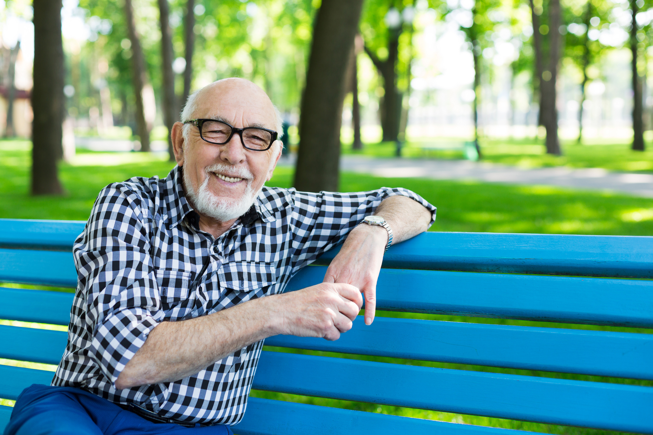 Smiling senior man sitting on blue bench outdoors.