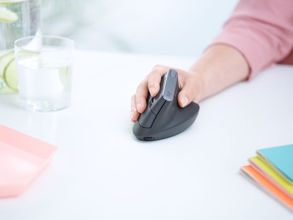 A hand holding a Logitech ergonomic mouse on a desk.