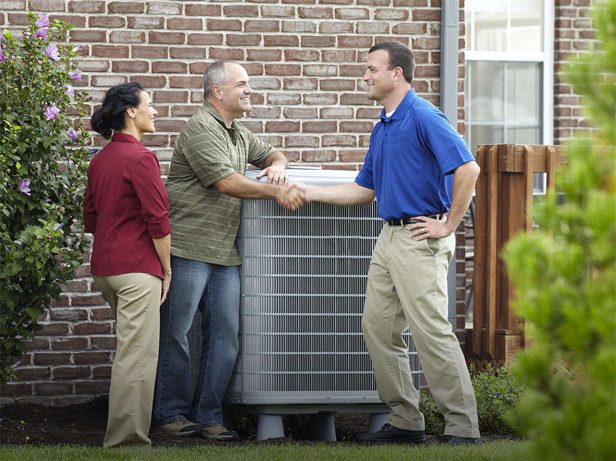 Two people shaking hands in front of an air conditioner at the side of a house, with a third person watching.