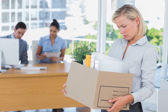 Woman with sad expression carrying cardboard box of office supplies