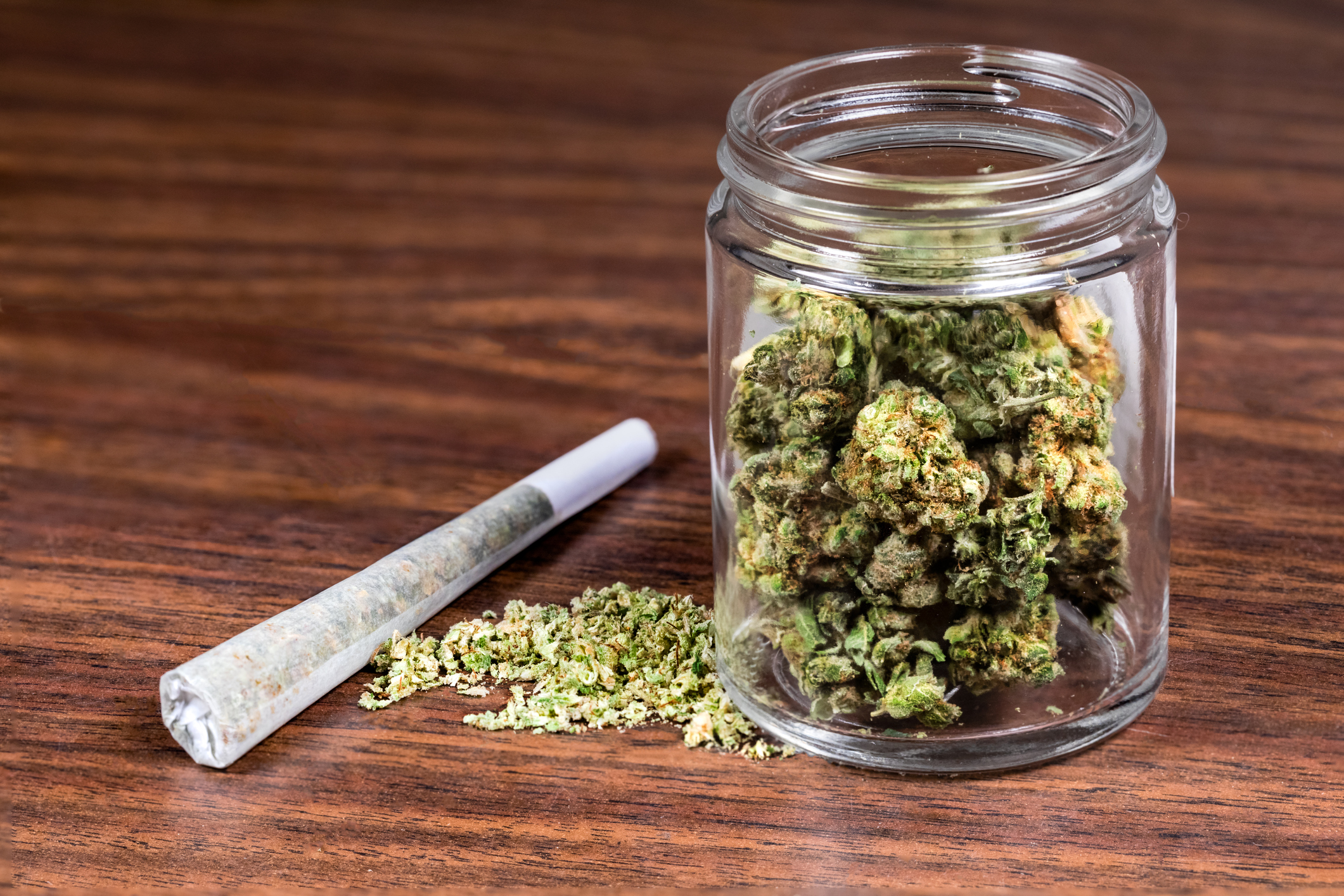 Jar containing marijuana buds sitting on a wooden table.