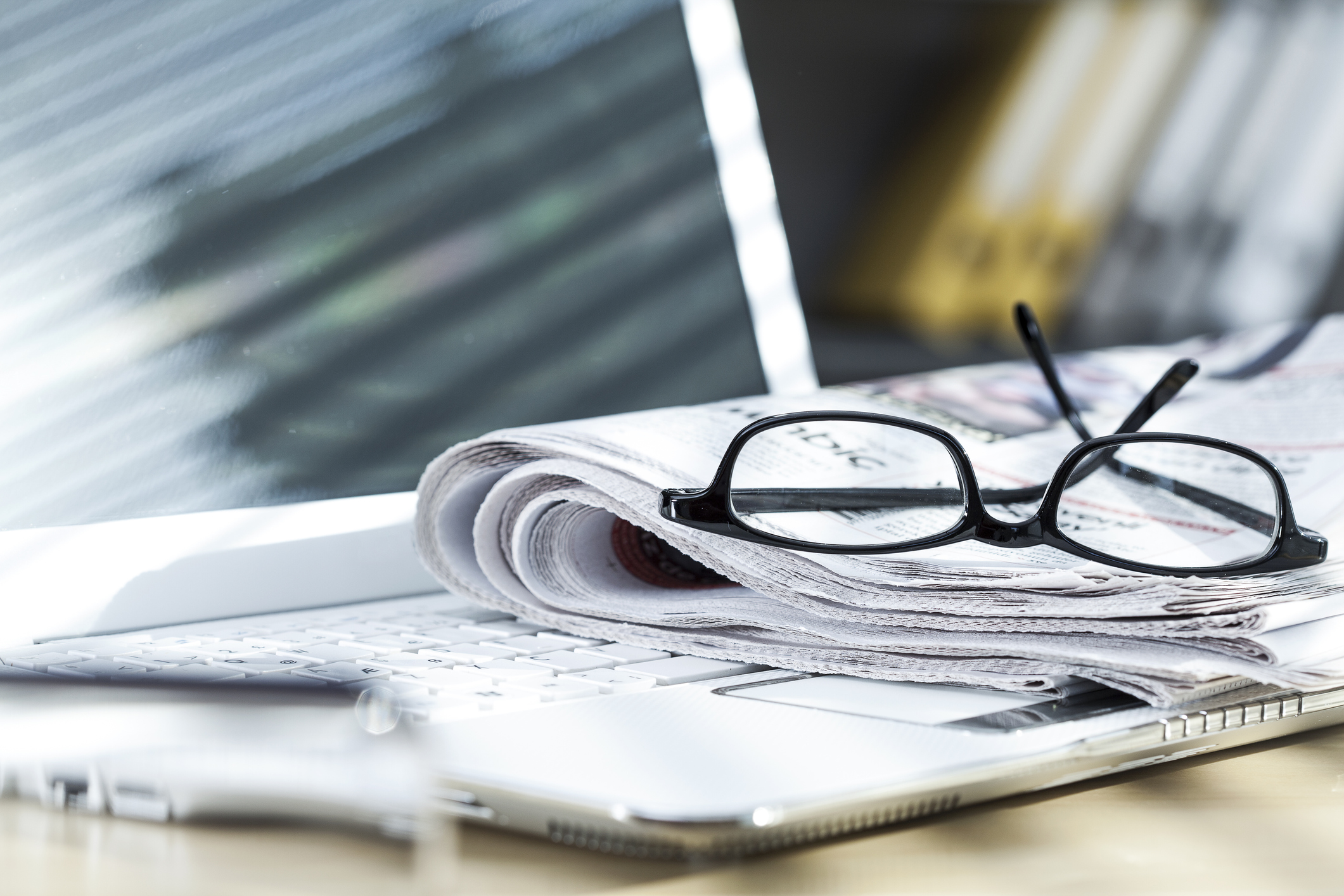 Folded newspaper and reading glasses resting on a laptop.