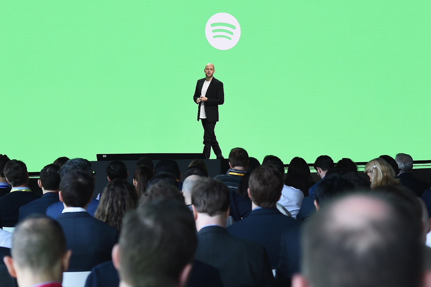 Daniel Ek on a stage in front of a green screen with the Spotify logo on it, in front of a crowd.