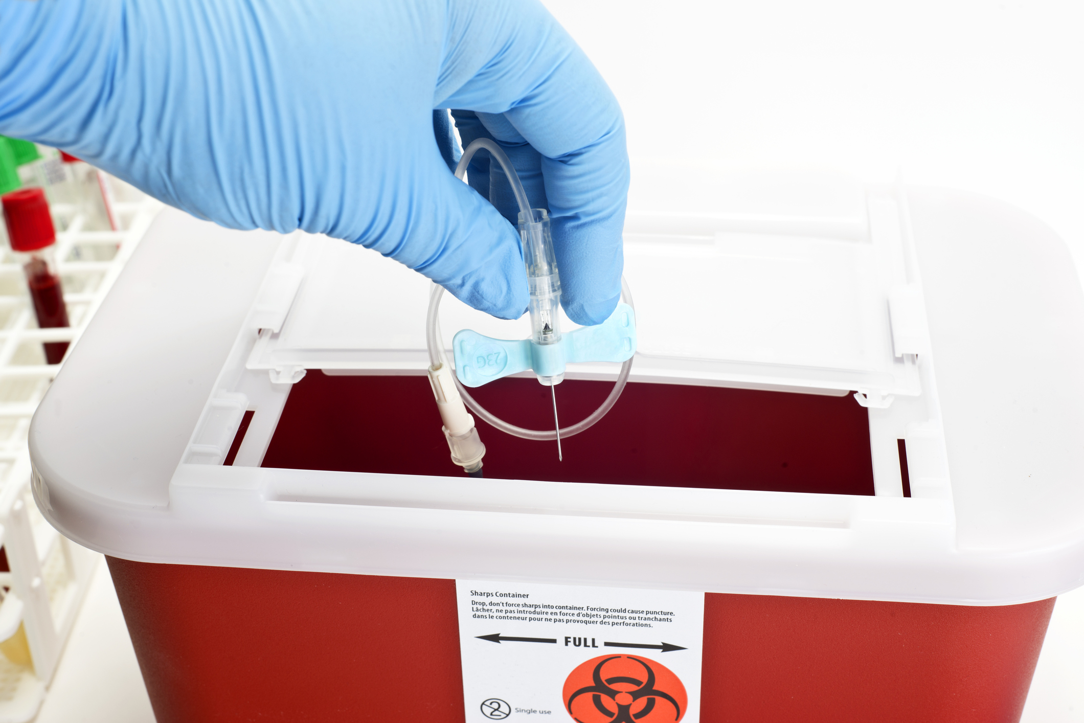 A gloved hand disposing medical waste in a container.