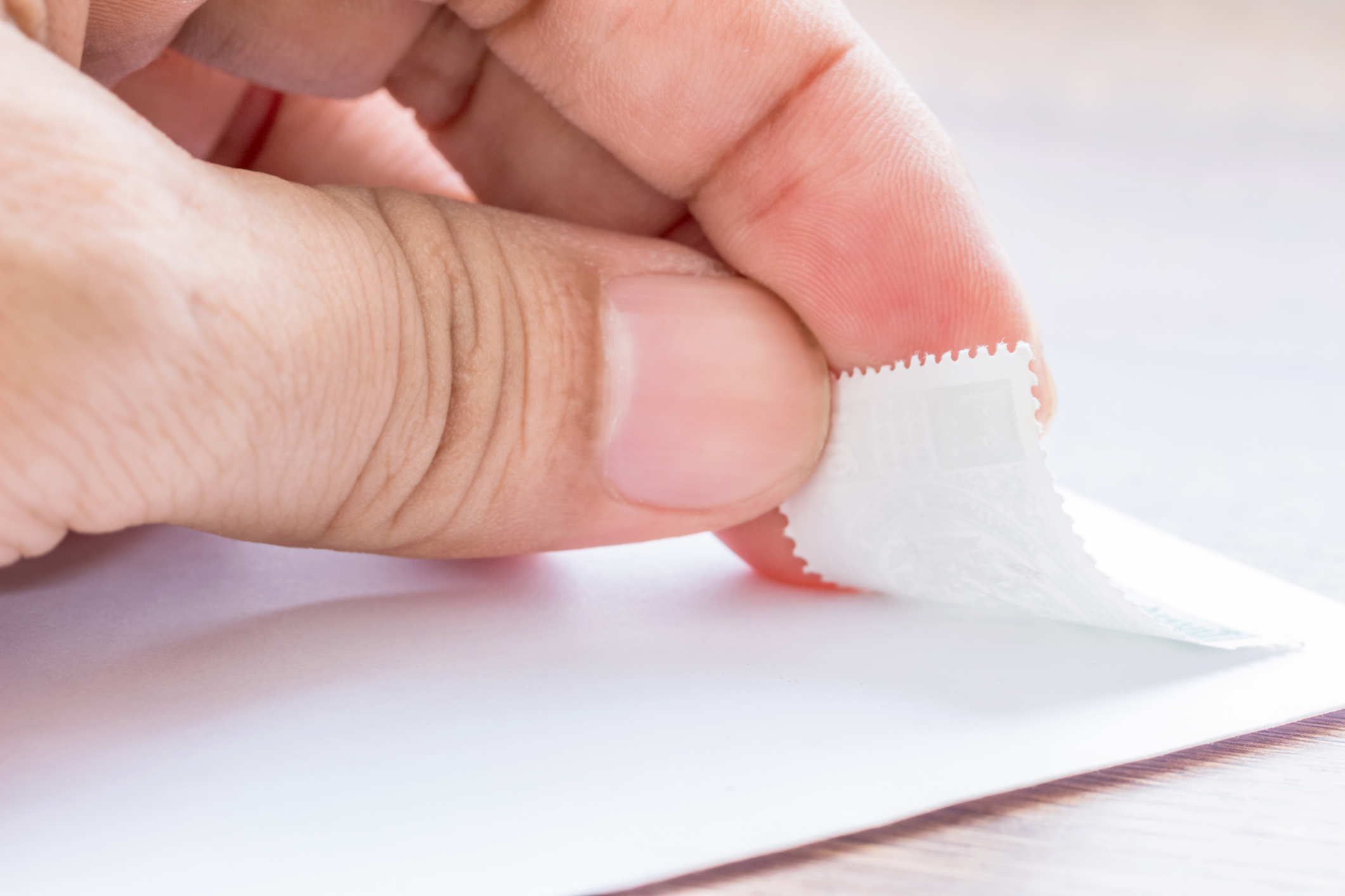 Hand putting a stamp on a white envelope