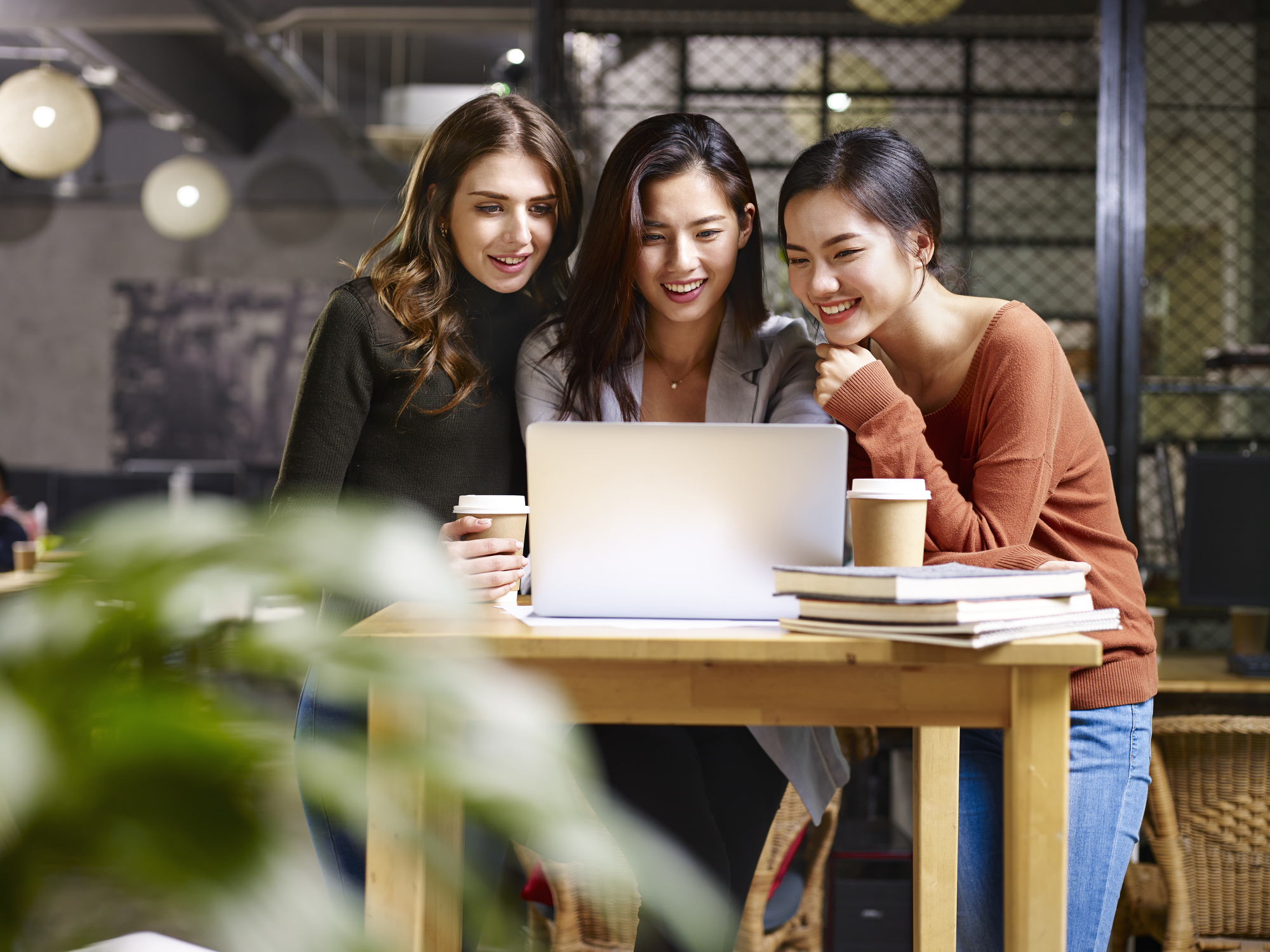 Three young women use a laptop in a coffee shop.