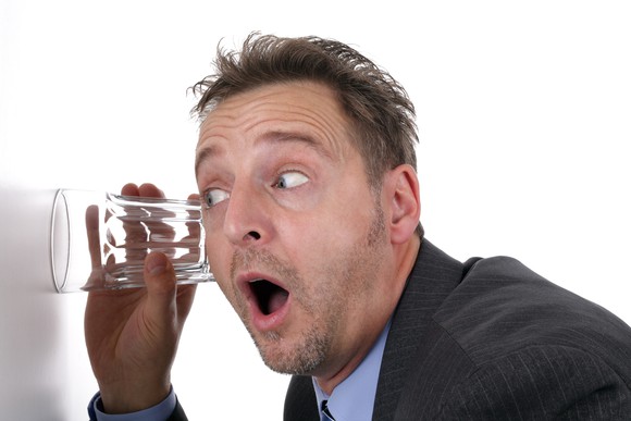 A man listens through a wall using a glass.
