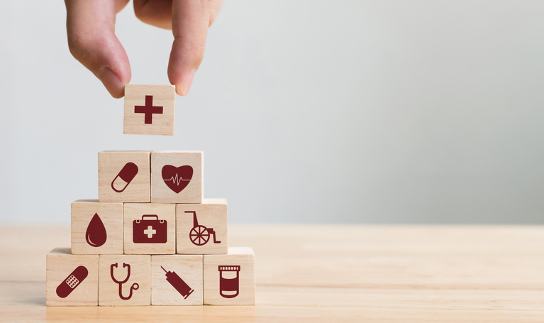 A hand placing blocks with medical icons on them into a pyramid.