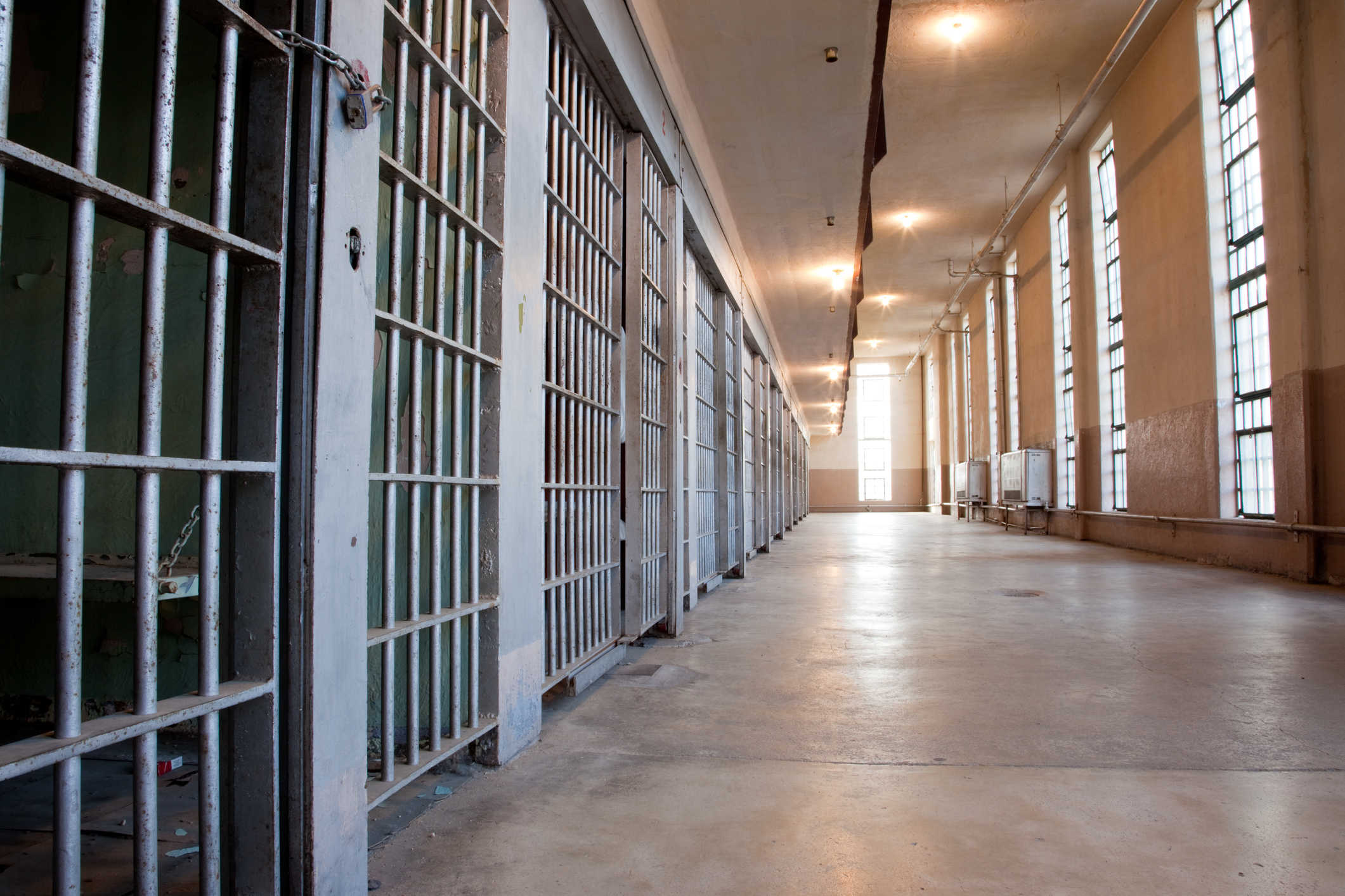 A long hallway in a prison with a row of cells to the left.