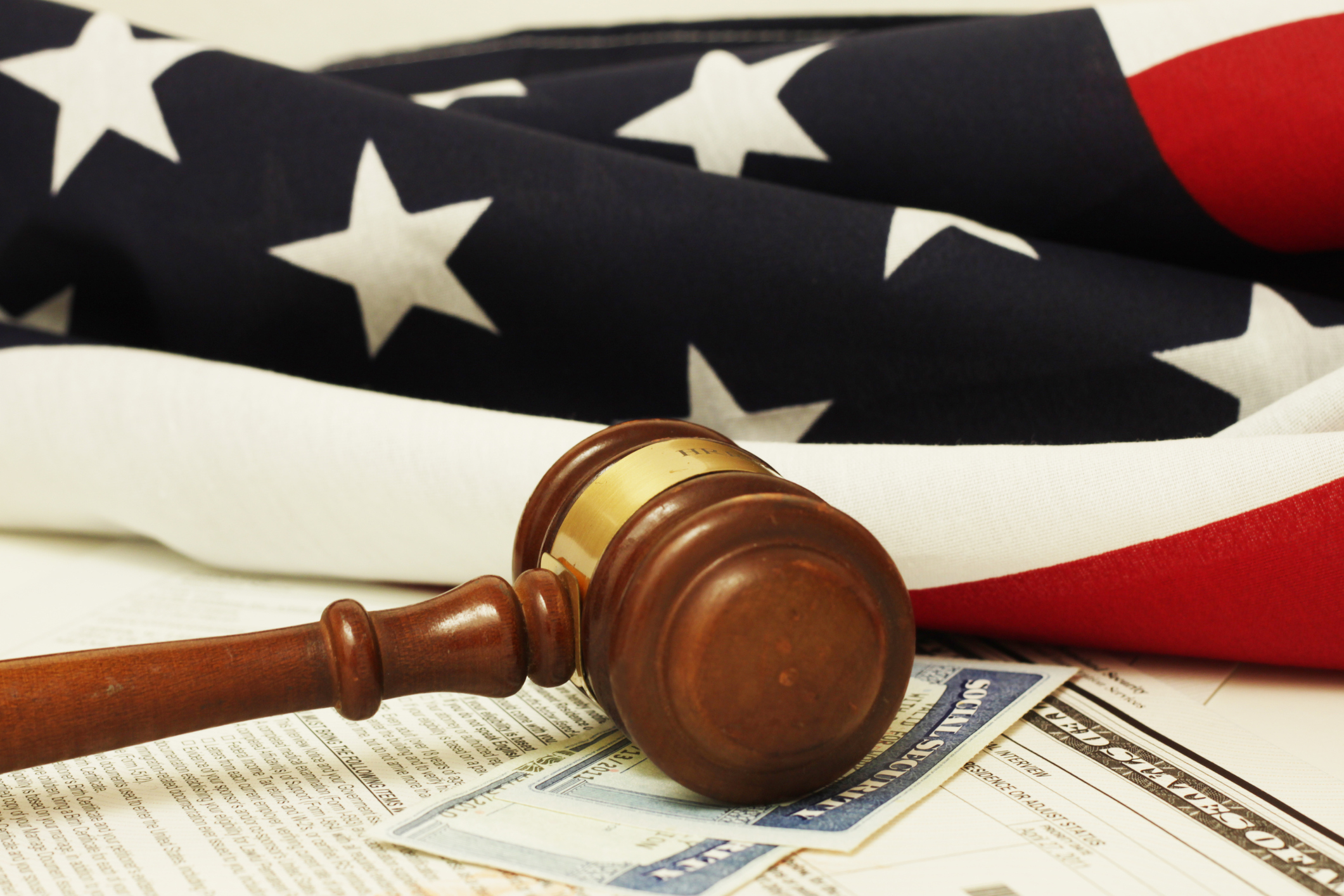 A judge's gavel lying atop two Social Security cards, and in front of an American flag.