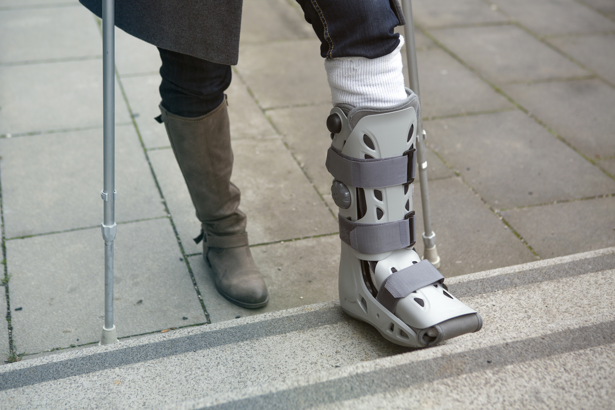 Legs only of a woman wearing a foot brace and using crutches.