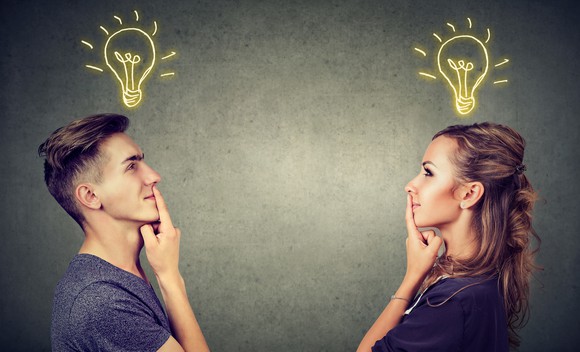 A man and woman facing each other, holding their fingers to their lips with light bulbs shining brightly above them.