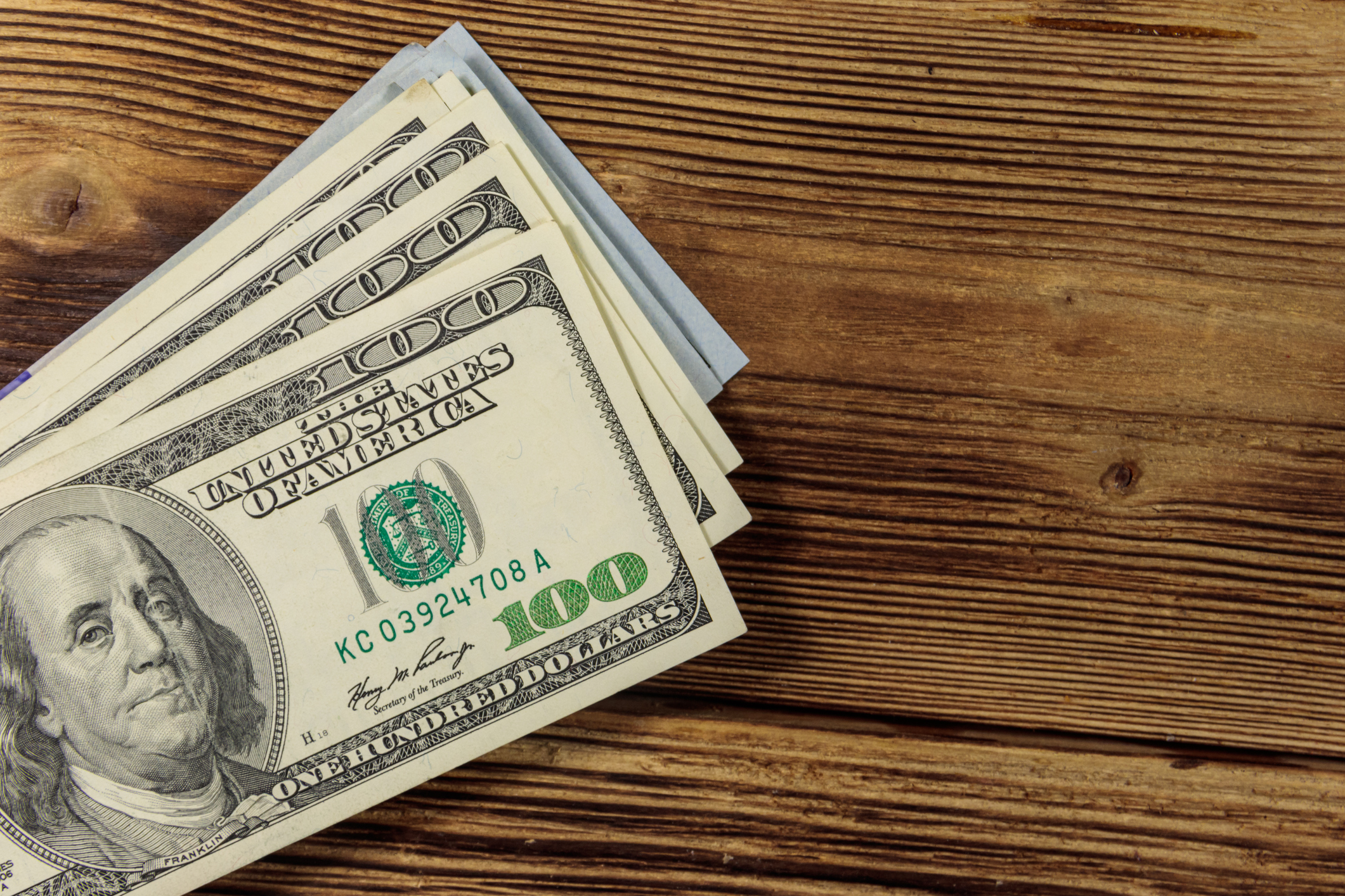Stack of hundred-dollar bills on wooden surface.