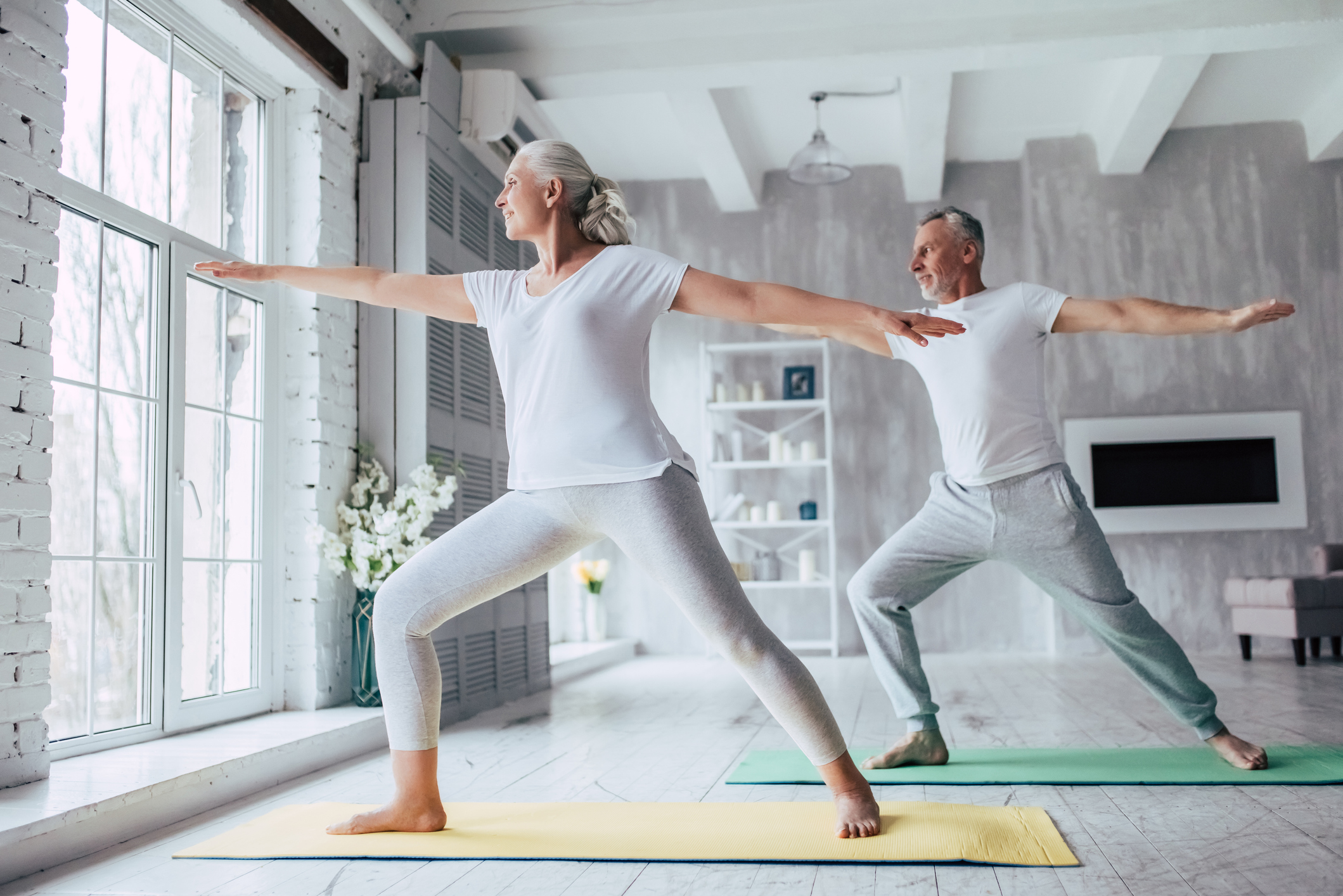 A senior couple doing yoga on mats in their home. 