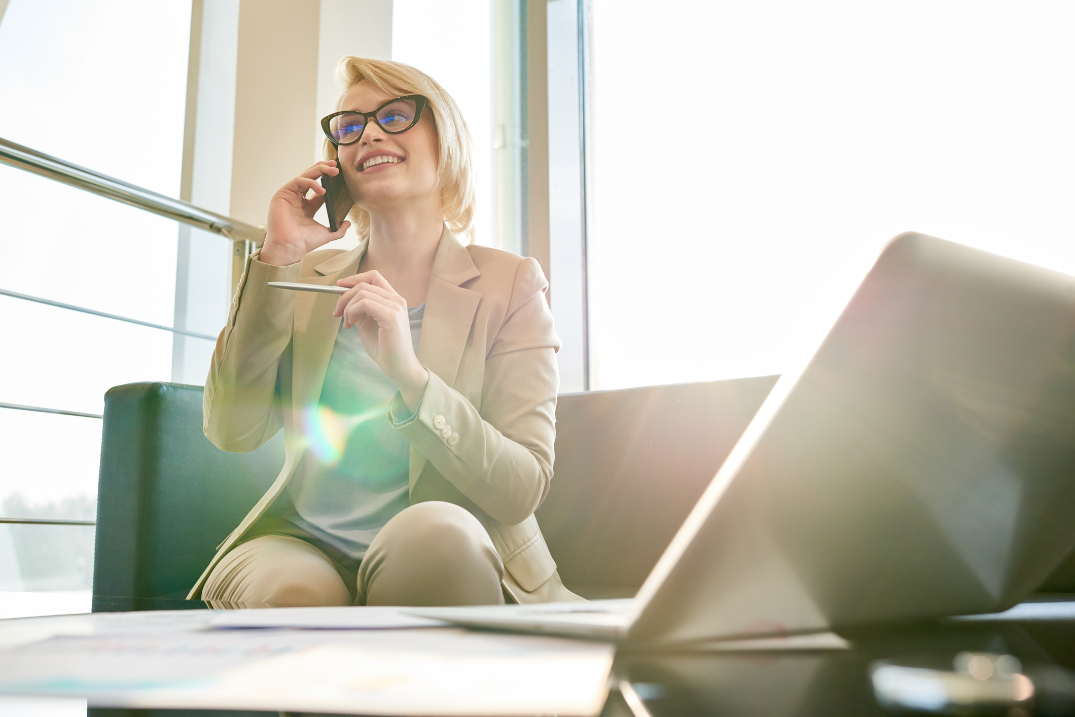 A woman sits on a couch talking on a cellphone, with an open laptop in the foreground