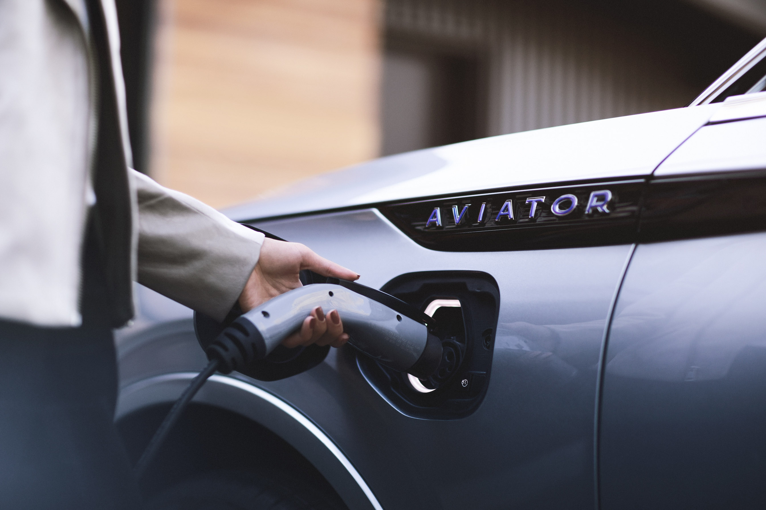 A close-up of the 2019 Lincoln Aviator Grand Touring's charging port. A man is shown holding a charging plug.