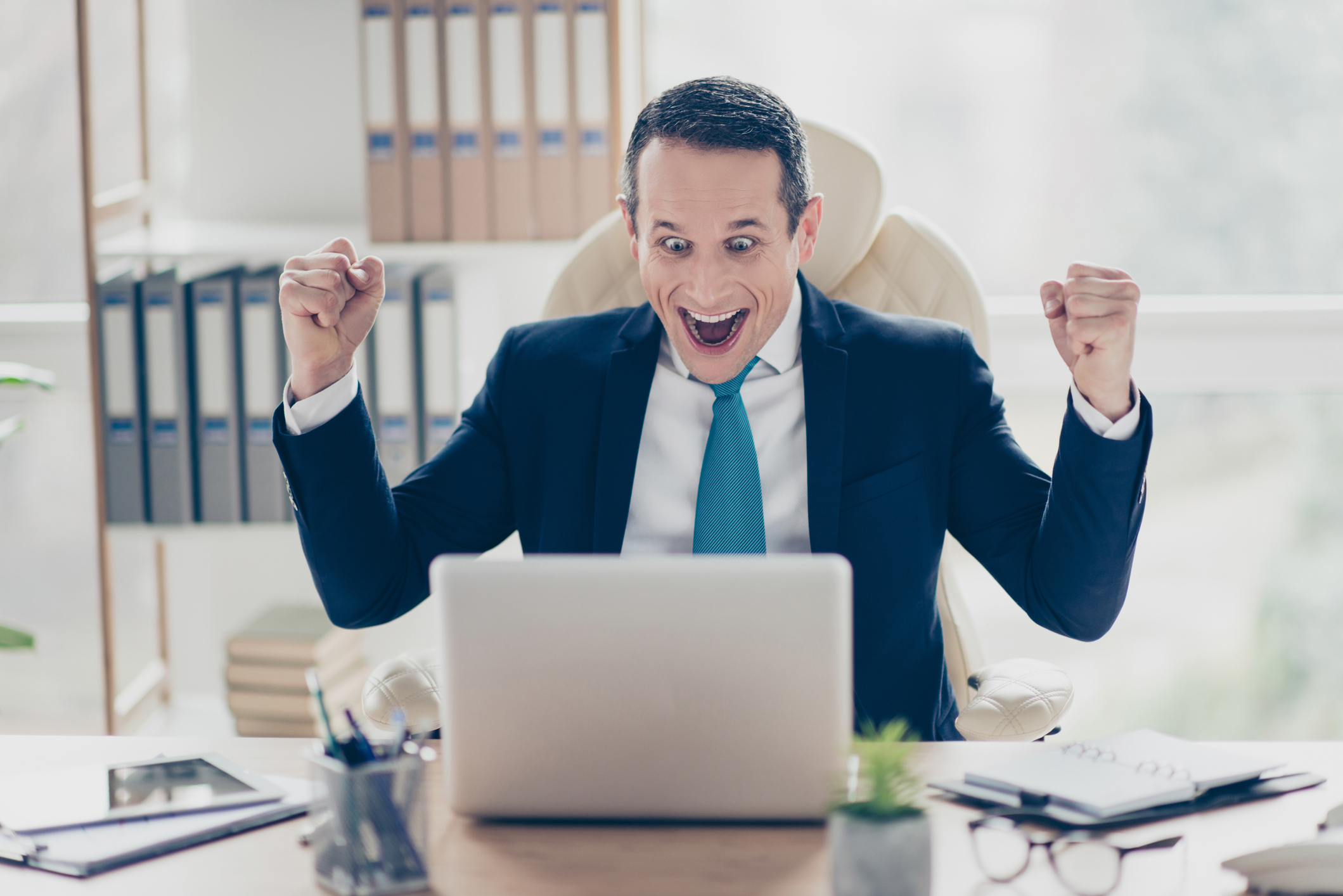 Man at laptop smiling and raising arms excitedly