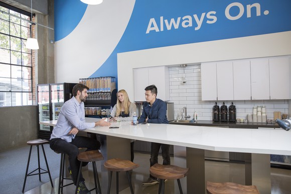 Employees sit around a table in the break room at Okta