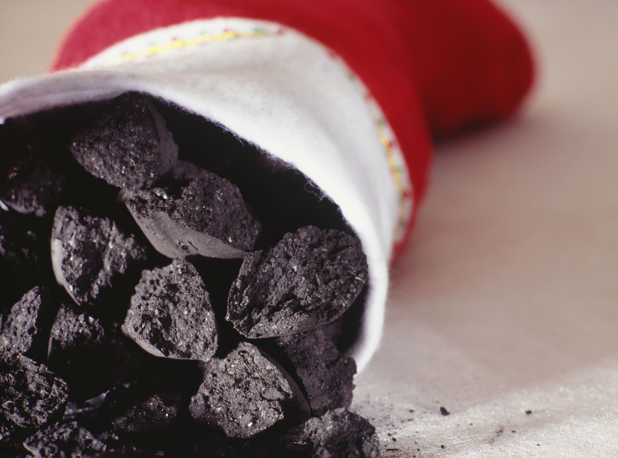 A close-up of lumps of coal being placed inside of a Christmas stocking.