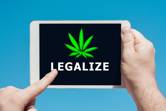 A person holding a tablet and touching the screen with shows a cannabis leaf and says the word Legalize. 