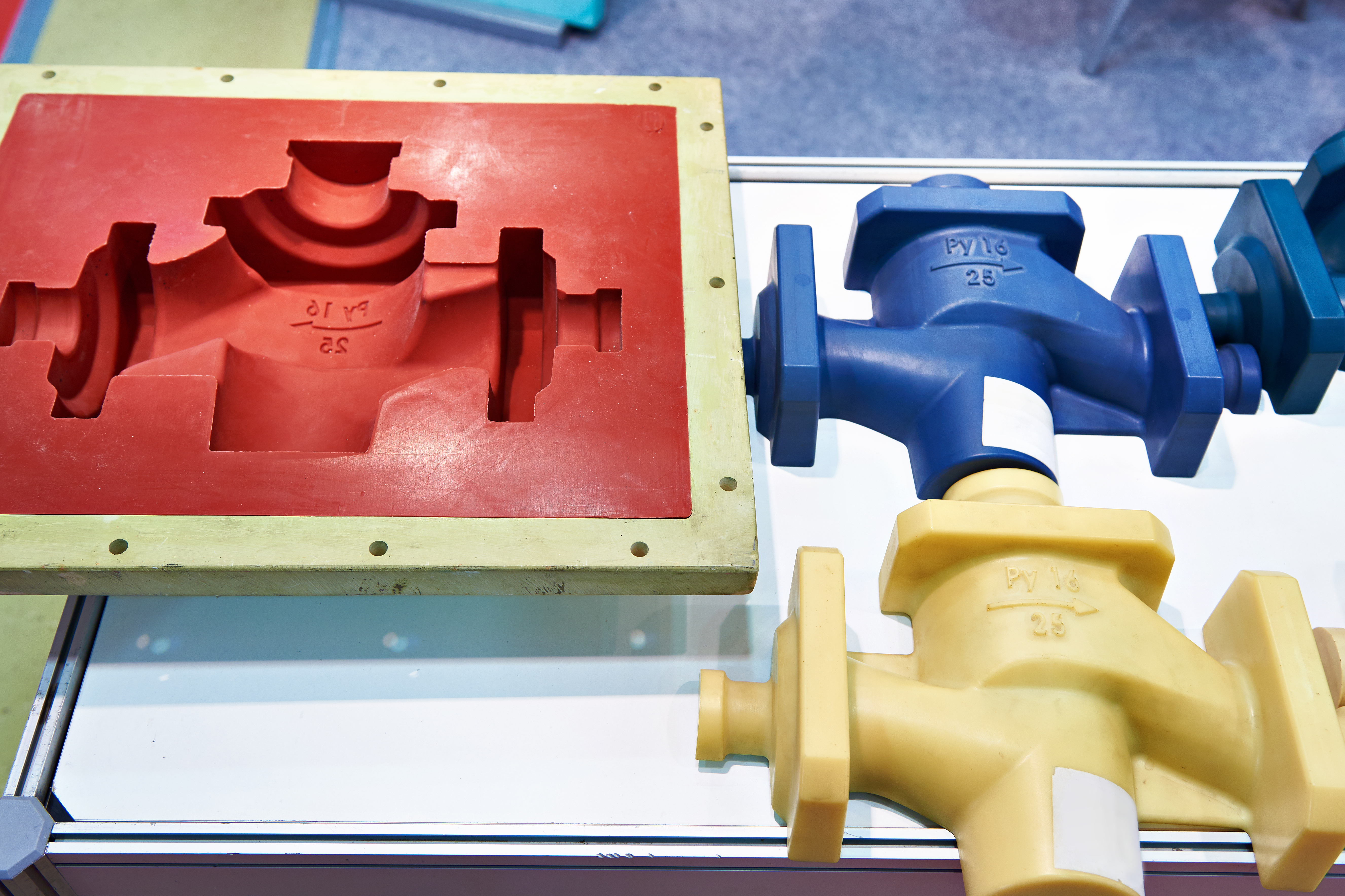Molds for casting industrial plastic valves side-by-side with two valves, in blue and yellow