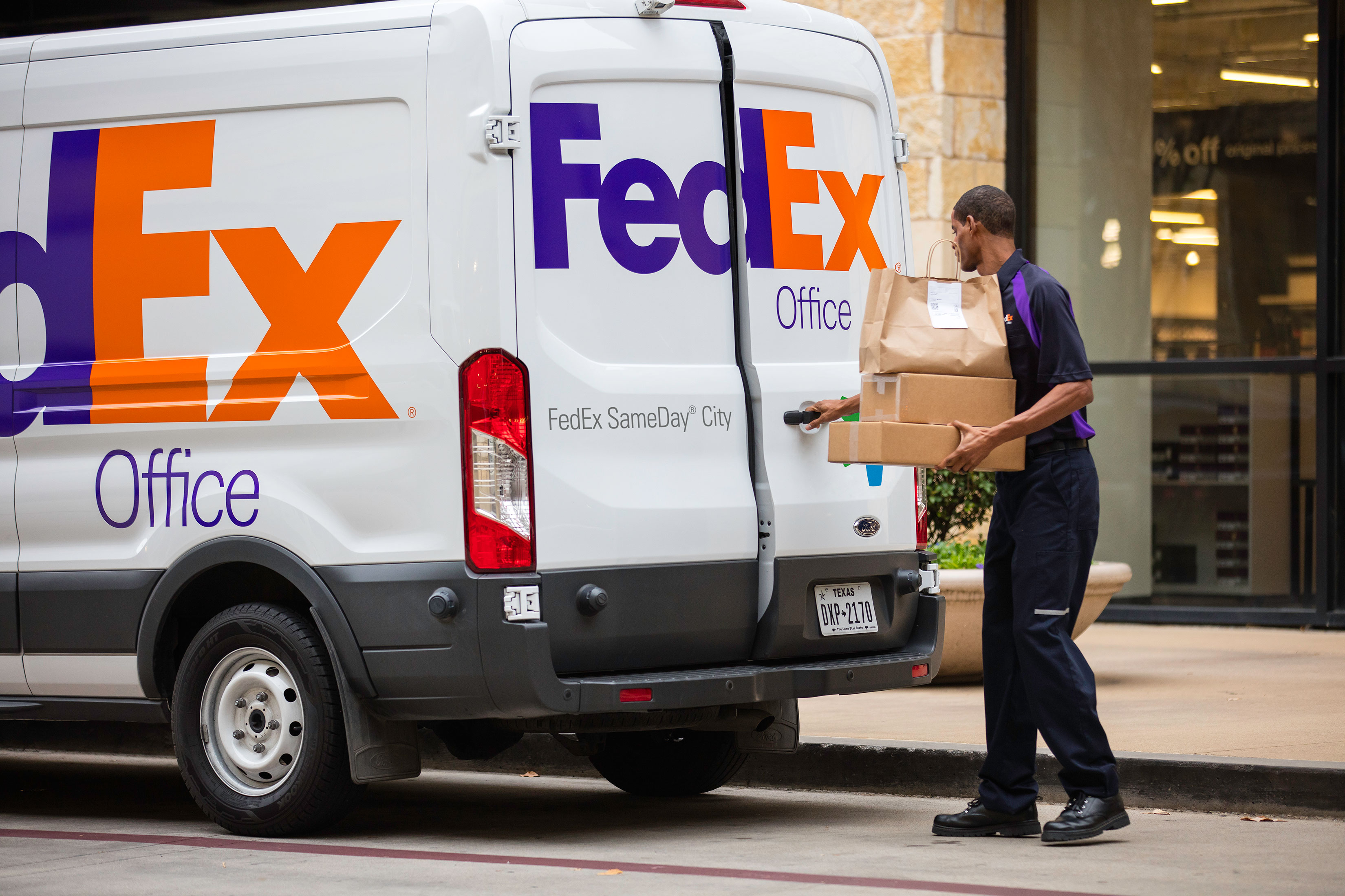 Person carrying package near back of van marked FedEx Office.