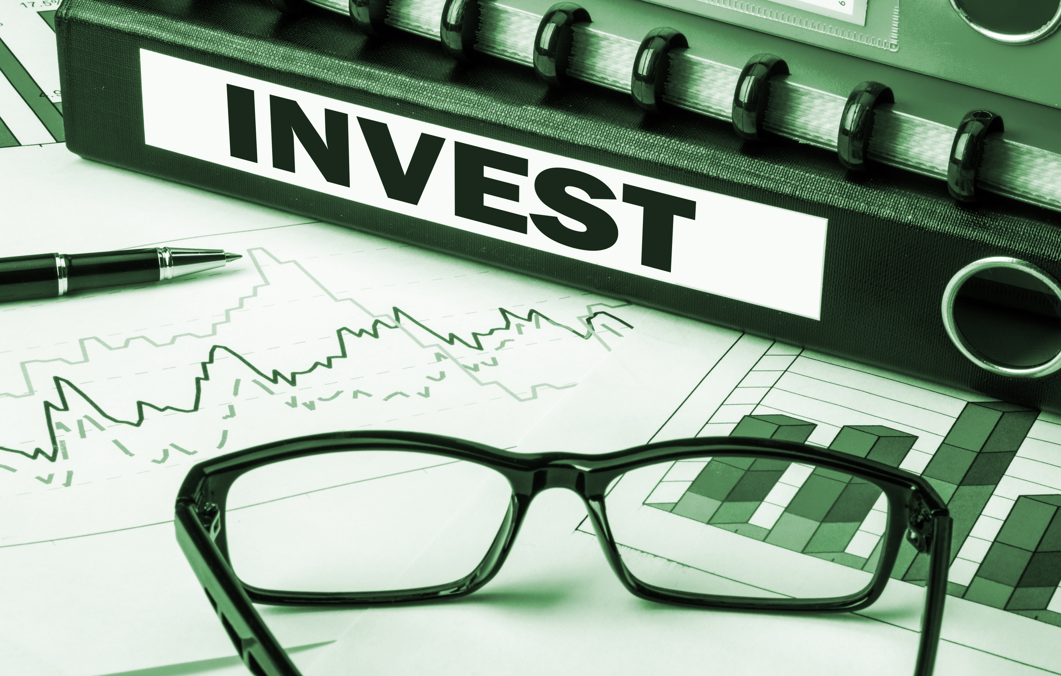Binder labeled Invest with glasses, pen, and graphs on a piece of paper.