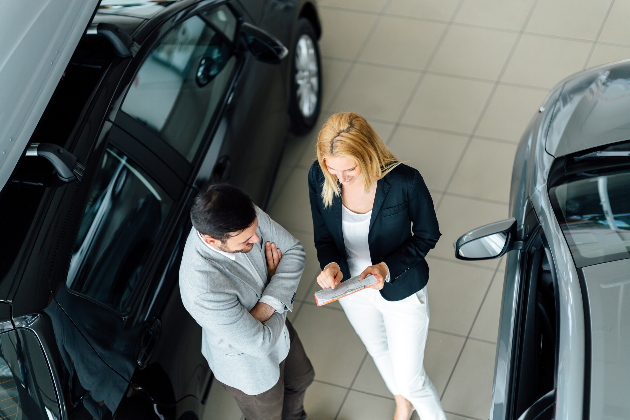 A male customer talking to a saleswoman in a car showroom.
