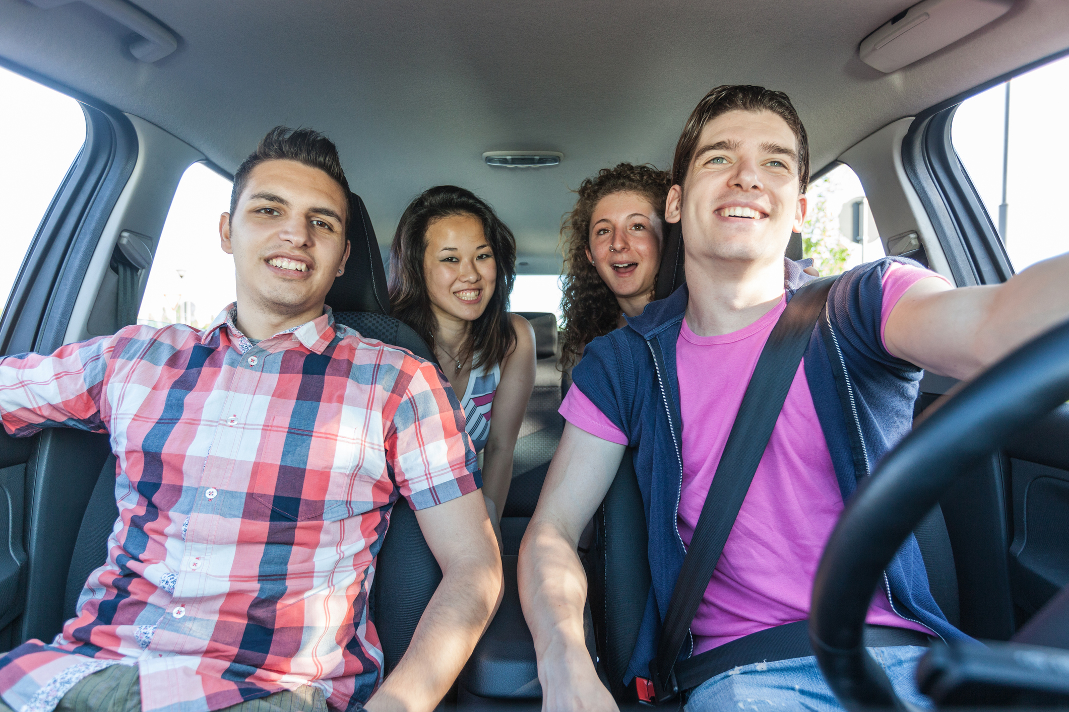 Four teenagers, two boys and two girls, are in a car, with one at the wheel.