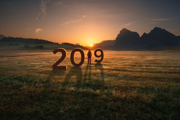 The numbers 2019 in a field with a person standing in place of the number 1 and the sun rising in the background.