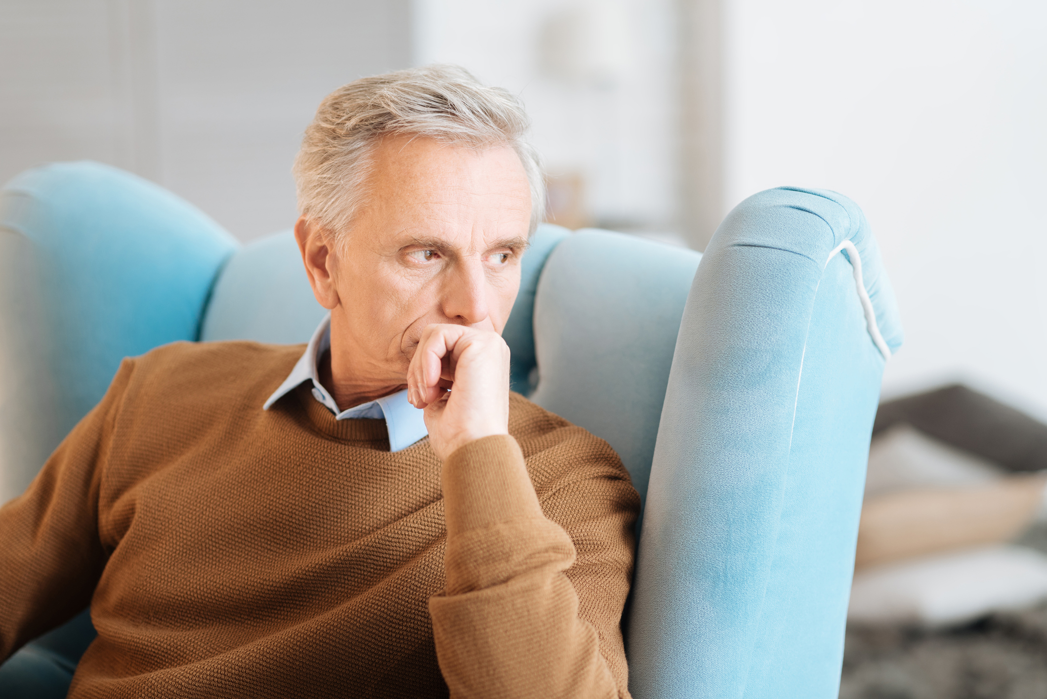 Older man deep in thought sitting in light-blue chair.