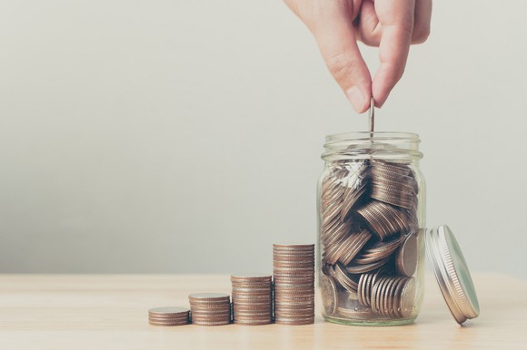 Hand placing U.S. quarter coin into a jar of coins.
