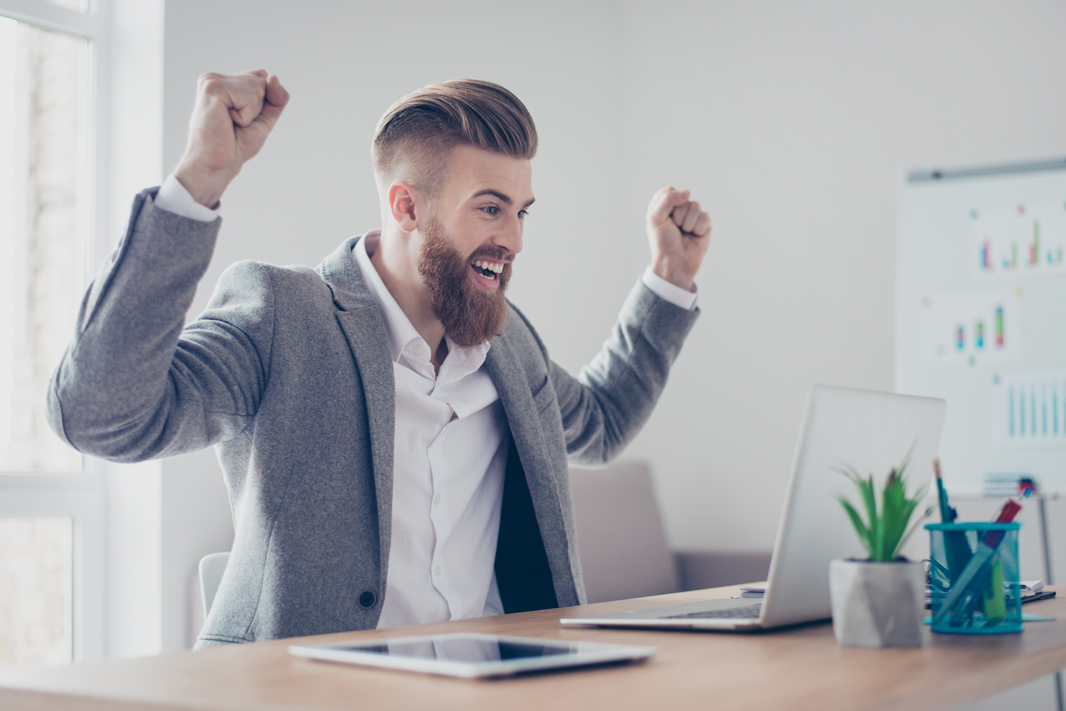 Man at laptop smiling and raising arms in celebration.